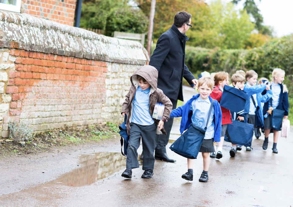 Image of students walking in single file outdoors with a teacher leading them on the side.